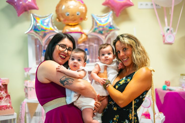 Fotógrafo de bautizos en Valencia. Dos chicas ríen con bebés en sus brazos en restaurante. Carlos Gimart Fotógrafo