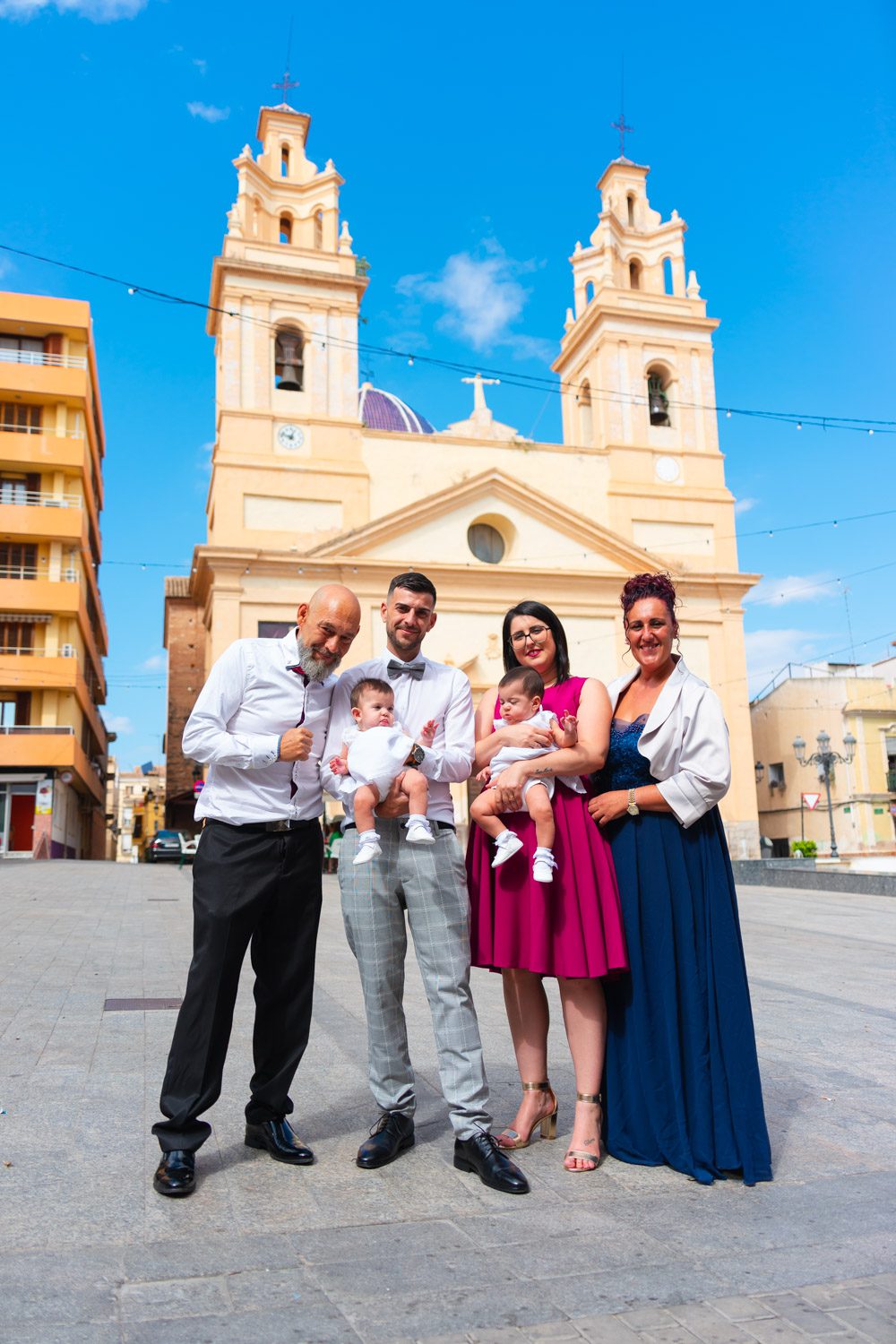 Familia posando con bebés delante de la iglesia del bautizo en pueblo de Valencia. Carlos Gimart Fotógrafo