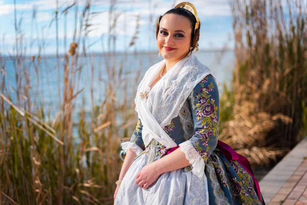 Sesión de fotos de fallera. Chica sonríe con vestido de fallera tradicional en paisaje bonito natural de Valencia durante las Fallas. Carlos Gimart Fotógrafo