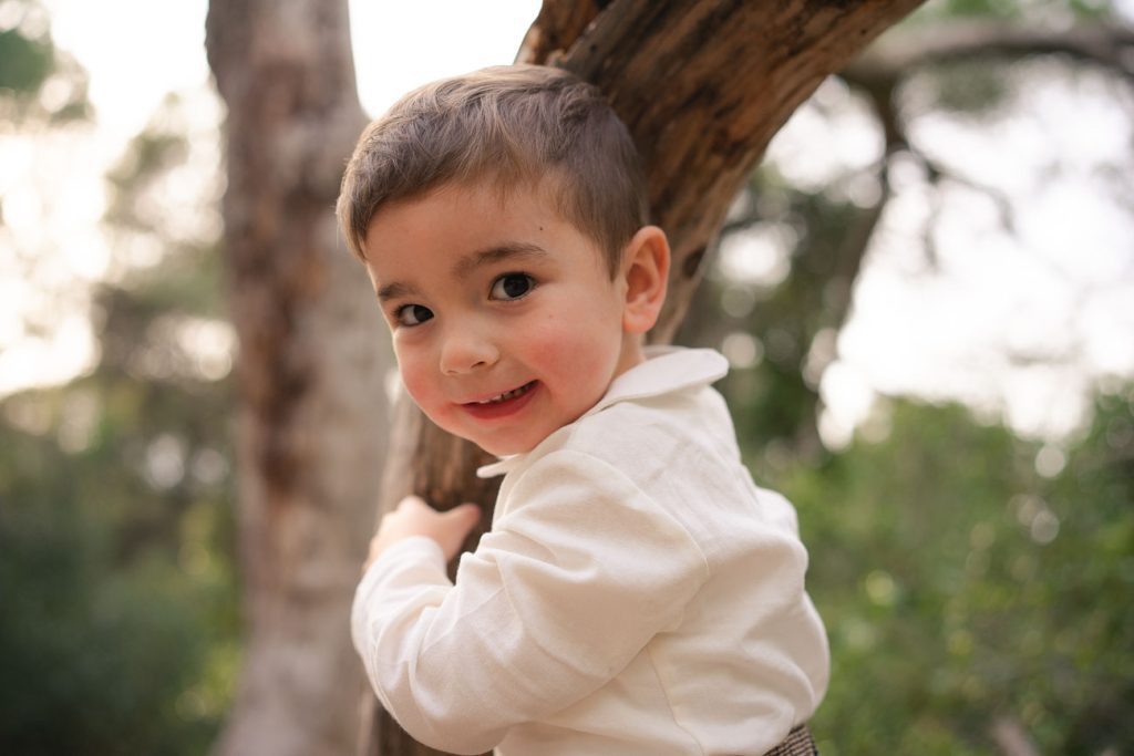 Niño pequeño ríe y juega entre los árboles del bosque. Carlos Gimart Fotógrafo.
