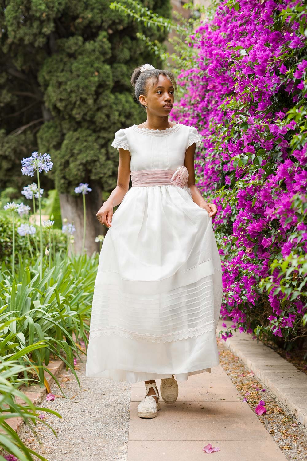 niña pasea con su traje de comunión rodeada de flores coloridas