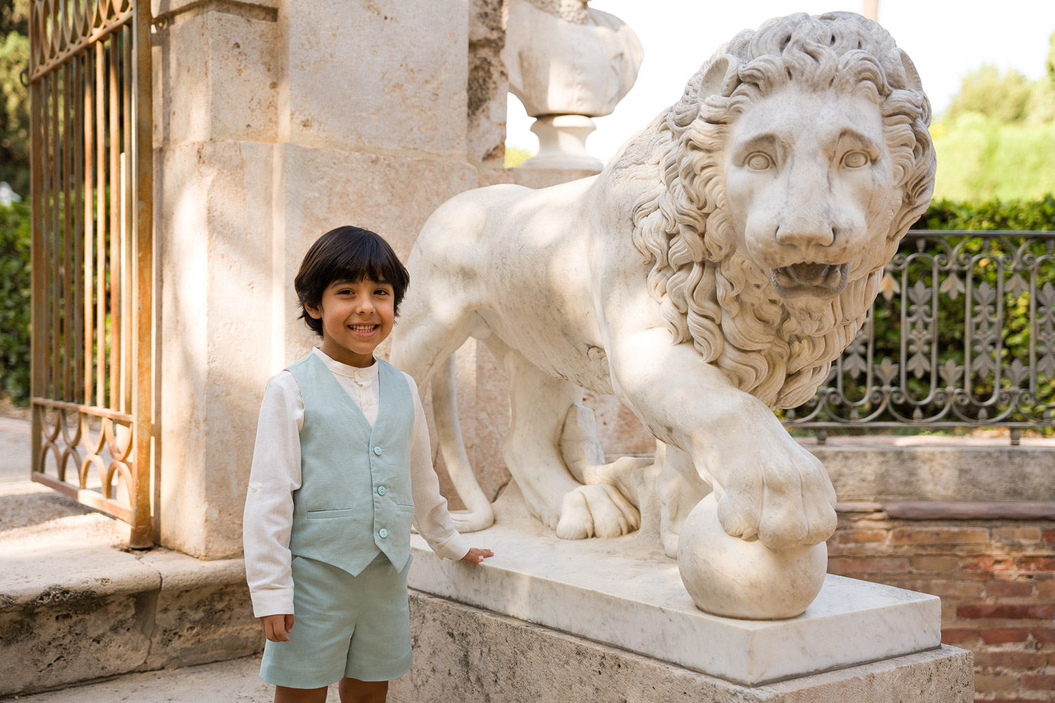 niño sonríe junto a estatua de león en Jardínes de Monforte